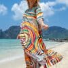 Paréo Long Multicolore aux Motifs Vibrants porté par une femme avec un chapeau et des lunettes au bord de la mer